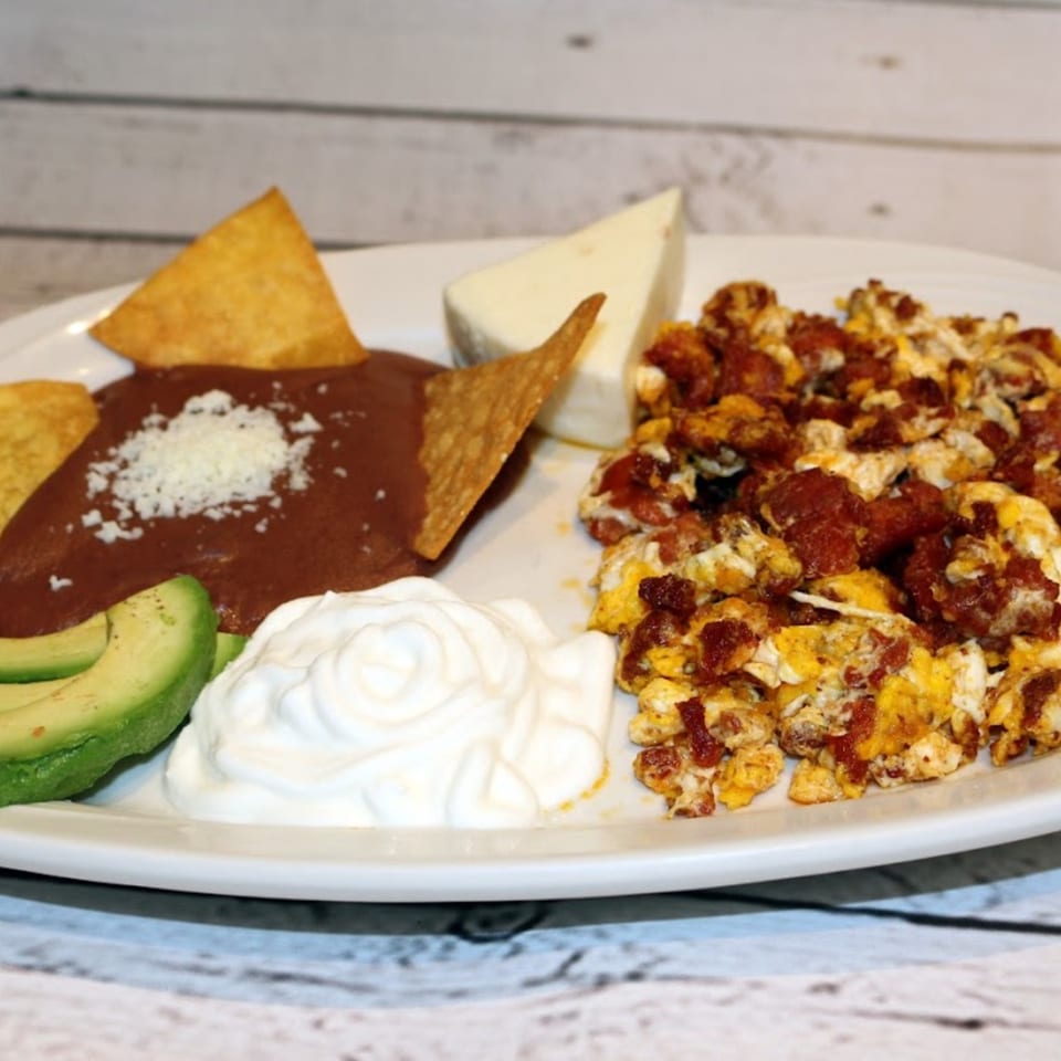 A Latin-American breakfast plate with scrambled eggs, refried beans, avocado, sour cream, and cheese.