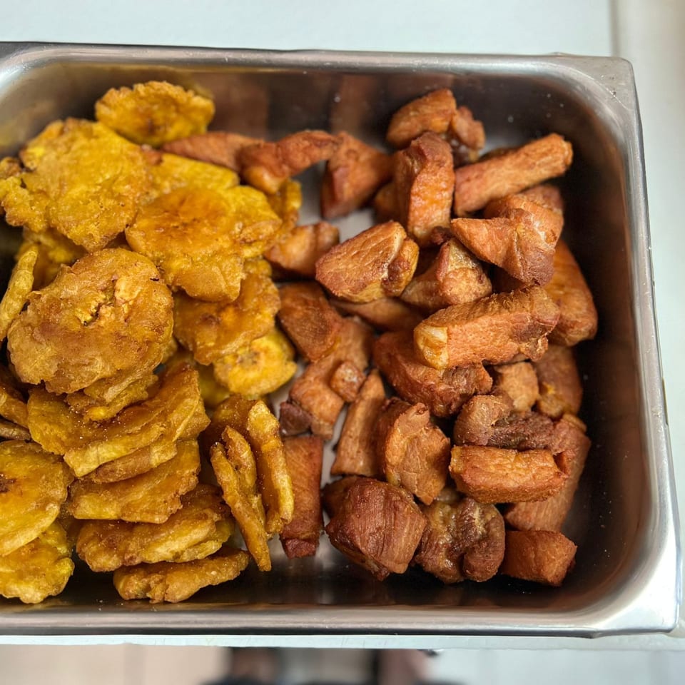 A metal tray filled with golden fried plantains and crispy fried pork chunks from El Rinconcito Latin Food.