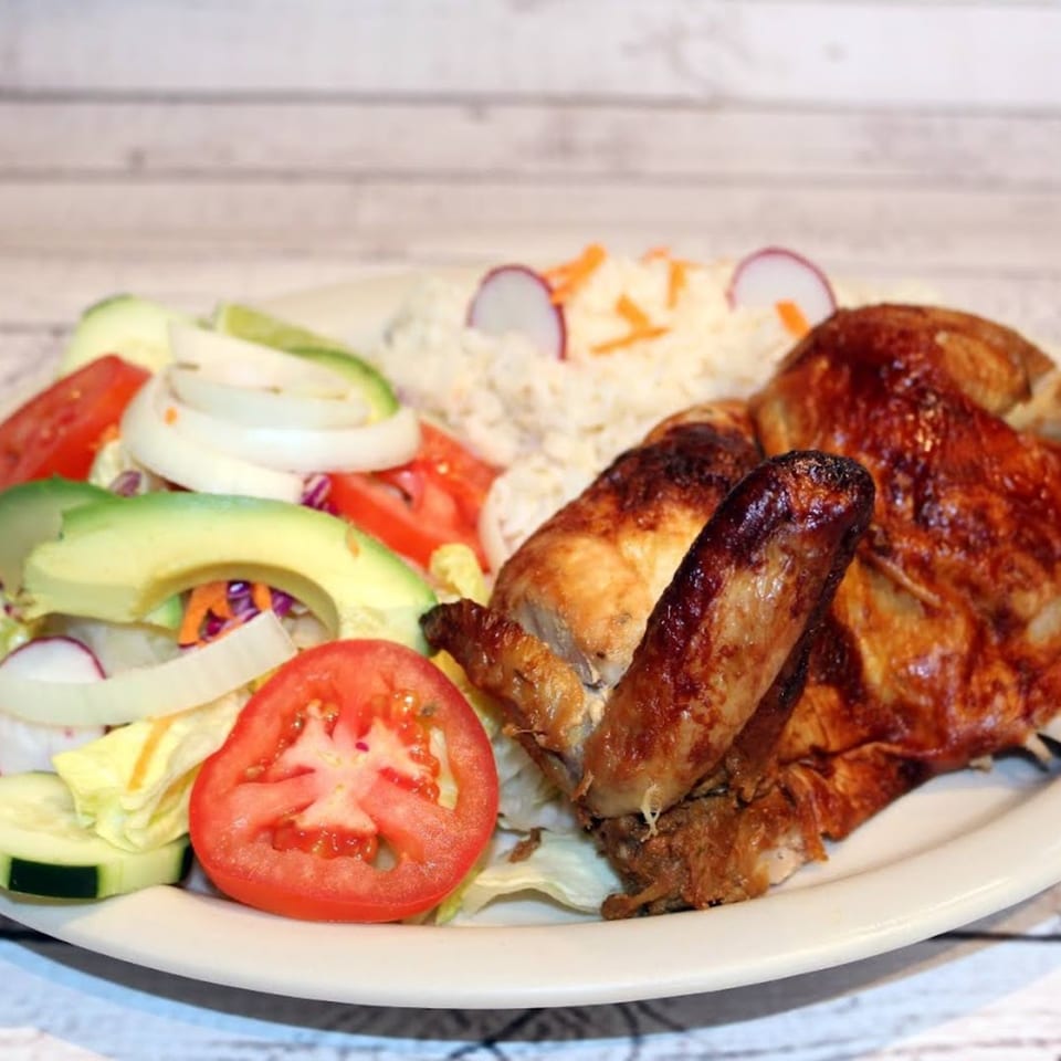 Roasted chicken with rice, avocado, tomatoes, onions, and cucumbers on a white plate.