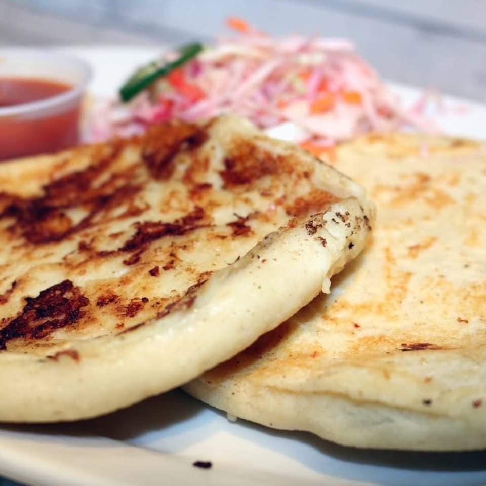 Two golden-brown pupusas with a side of red sauce and curtido on a white plate.