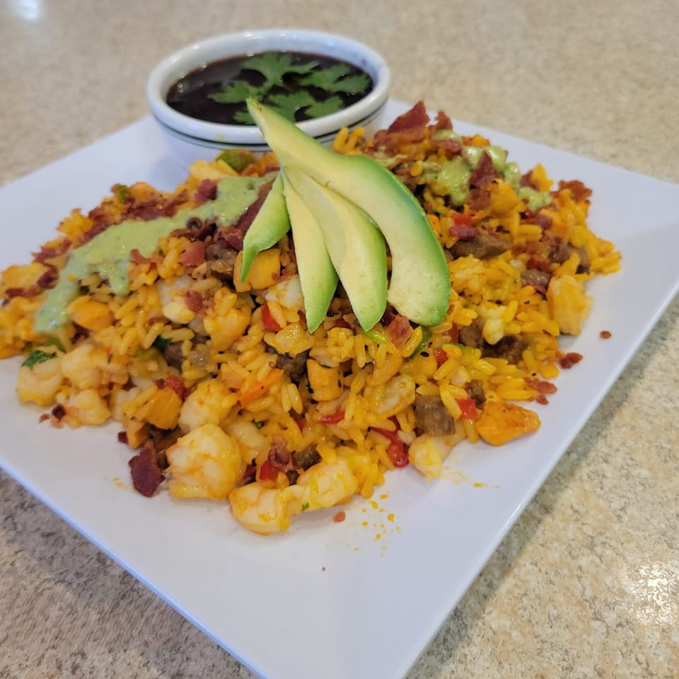 Latin-American rice dish with shrimp, bacon, avocado, and green sauce, served with a side of black beans.