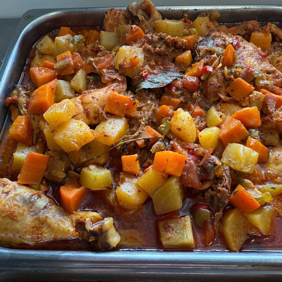 A large metal tray filled with Latin-American chicken stew, potatoes, and carrots in a rich sauce.
