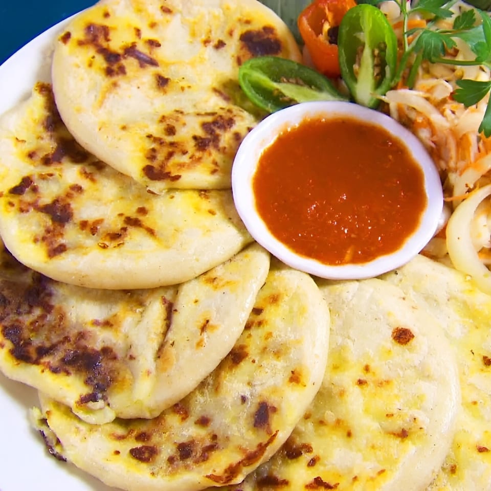 A plate of El Rinconcito's pupusas with curtido, salsa roja, and sliced peppers.